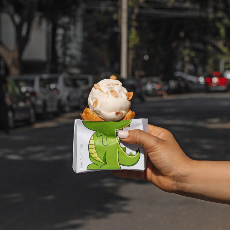 Helado servido en un dinocono de waffle con el fonde de una calle en un día soleado.