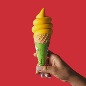 Helado soft serve Mango en cono, sobre fondo rojo vibrante.