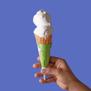 Mano sosteniendo un cono de helado de coco sobre un fondo azul